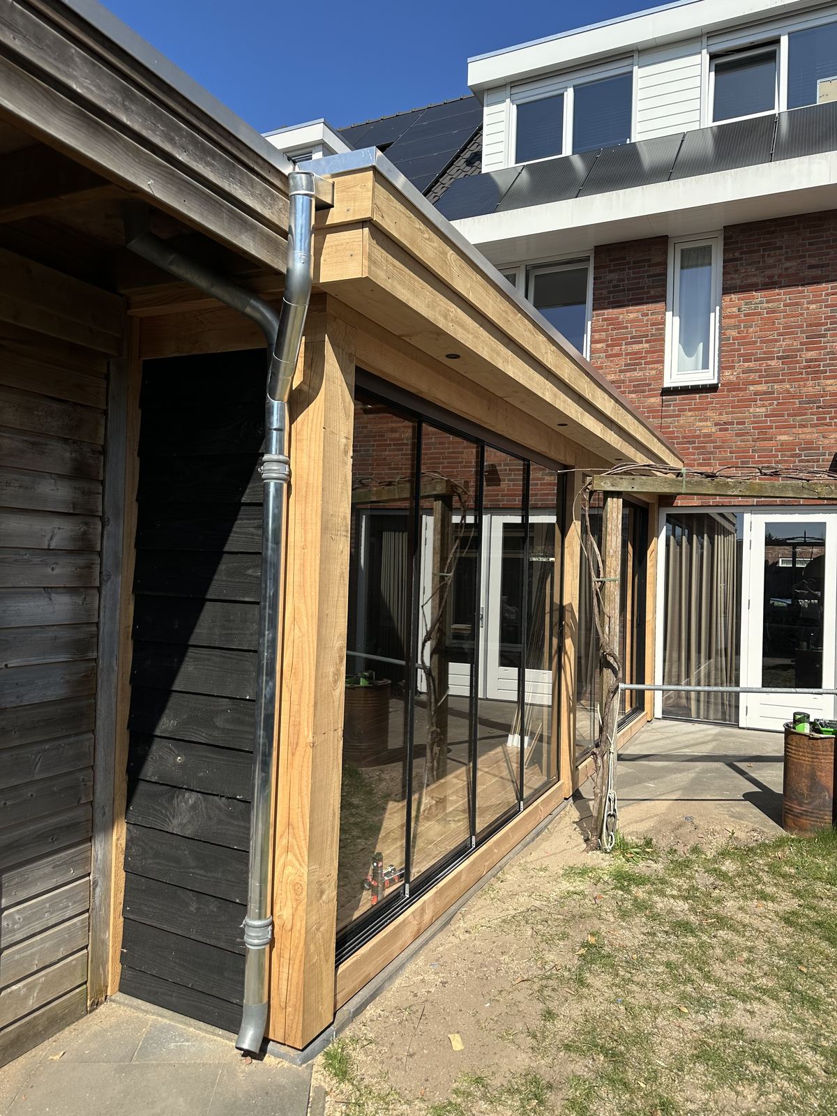 Zijkant overkapping met glazen schuifwand en regenpijp